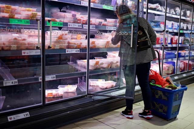 A customer looks at packages of chilled chicken cuts in a part-empty refrigerated display unit at a Lidl supermarket store