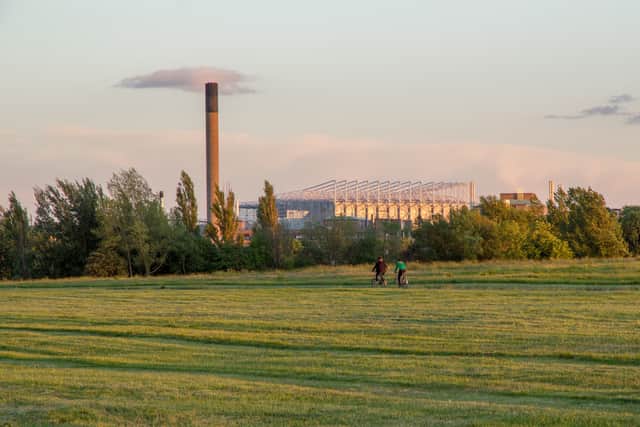 Friends cycle through Newcastle-Upon-Tyne’s Town Moor park with the impressive structure of St James Park football stadium looming large in the background.