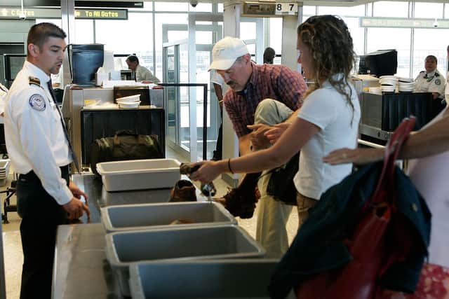 A passenger takes off his shoes as other passengers put their carry-on luggage in trays for x-ray inspection before they pass through a security check-point at Dulles International Airport. (Photo by Alex Wong/Getty Images)