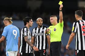 Robert Jones shows a yellow card to Sandro Tonali of Newcastle United during the Premier League match between Manchester City and Newcastle United at Etihad Stadium on August 19, 2023 in Manchester, England.