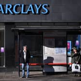 Commuters wait at a bus stop outside a branch of Barclays in London.