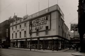 A view of the exterior of Fenwick's Blackett Street Newcastle upon Tyne taken in 1932. There is a large illuminated sign on the exterior 'We'll See Fenwick's First'. There is a lane to the right of Fenwick's with Emmerson Chambers on the opposite side. 