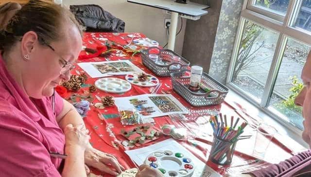 Staff member Joanne Stayman helps resident John Atkinson make items for the market