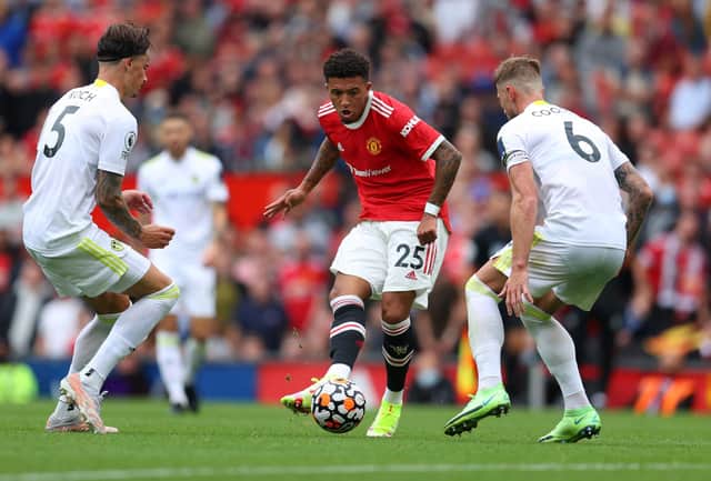 MANCHESTER, ENGLAND - AUGUST 14: Jadon Sancho of Manchester United passes the ball whilst under pressure from Robin Koch and Liam Cooper of Leeds United during the Premier League match between Manchester United  and  Leeds United at Old Trafford on August 14, 2021 in Manchester, England. (Photo by Catherine Ivill/Getty Images,)